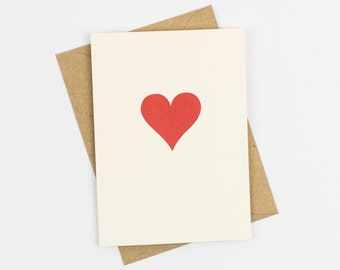 A white card with a red heart in the center sits on top of a light brown envelope